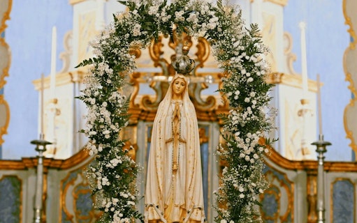 Statue of Our Lady of Fatima adorned with flowers in a church setting.