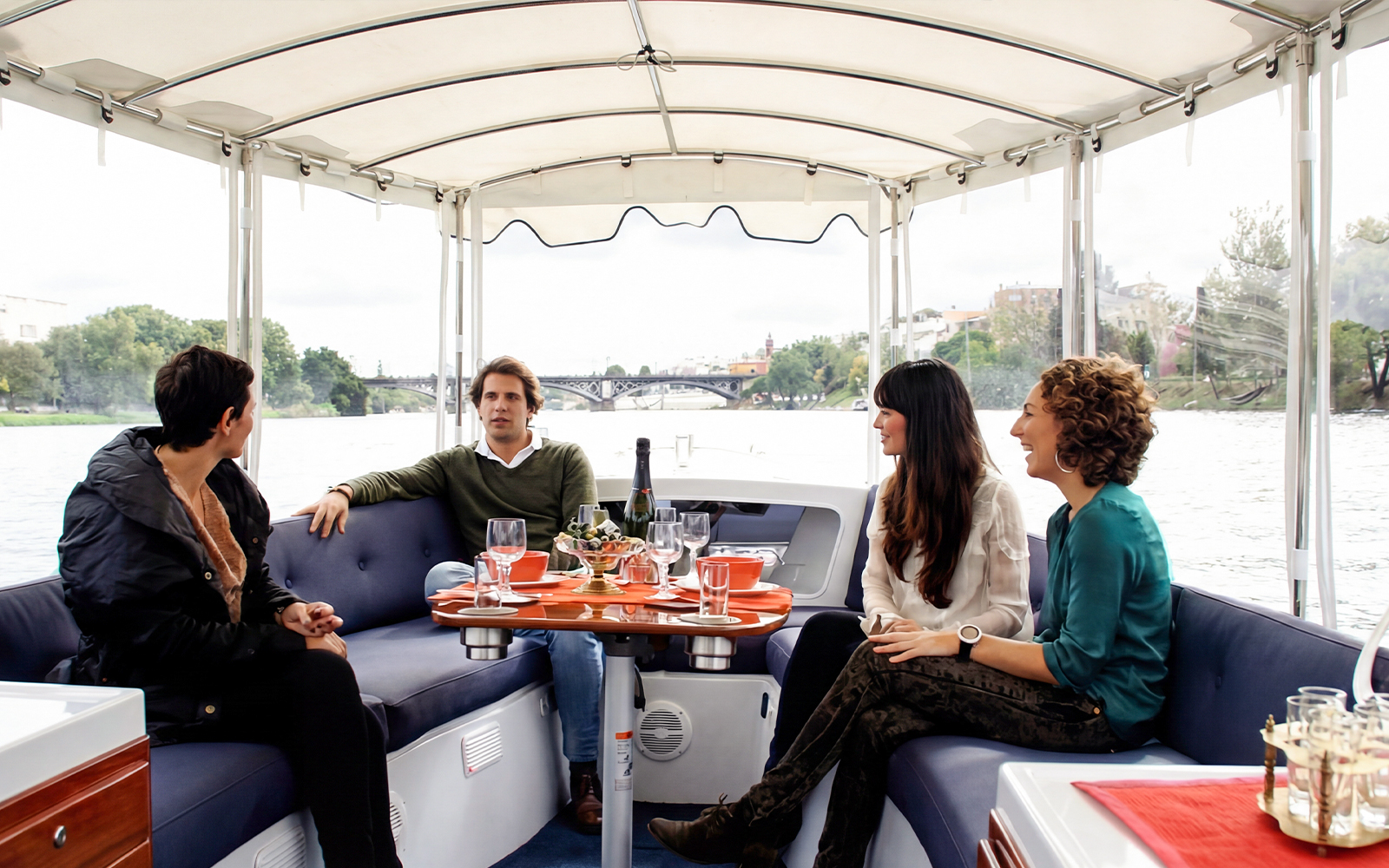 Tourists enjoying drinks and snacks on a Seville river cruise with city views.
