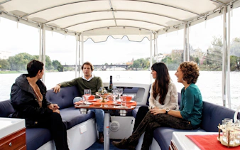 Tourists enjoying drinks and snacks on a Seville river cruise with city views.