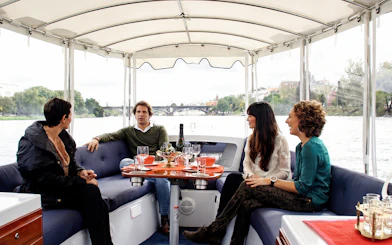 Tourists enjoying drinks and snacks on a Seville river cruise with city views.