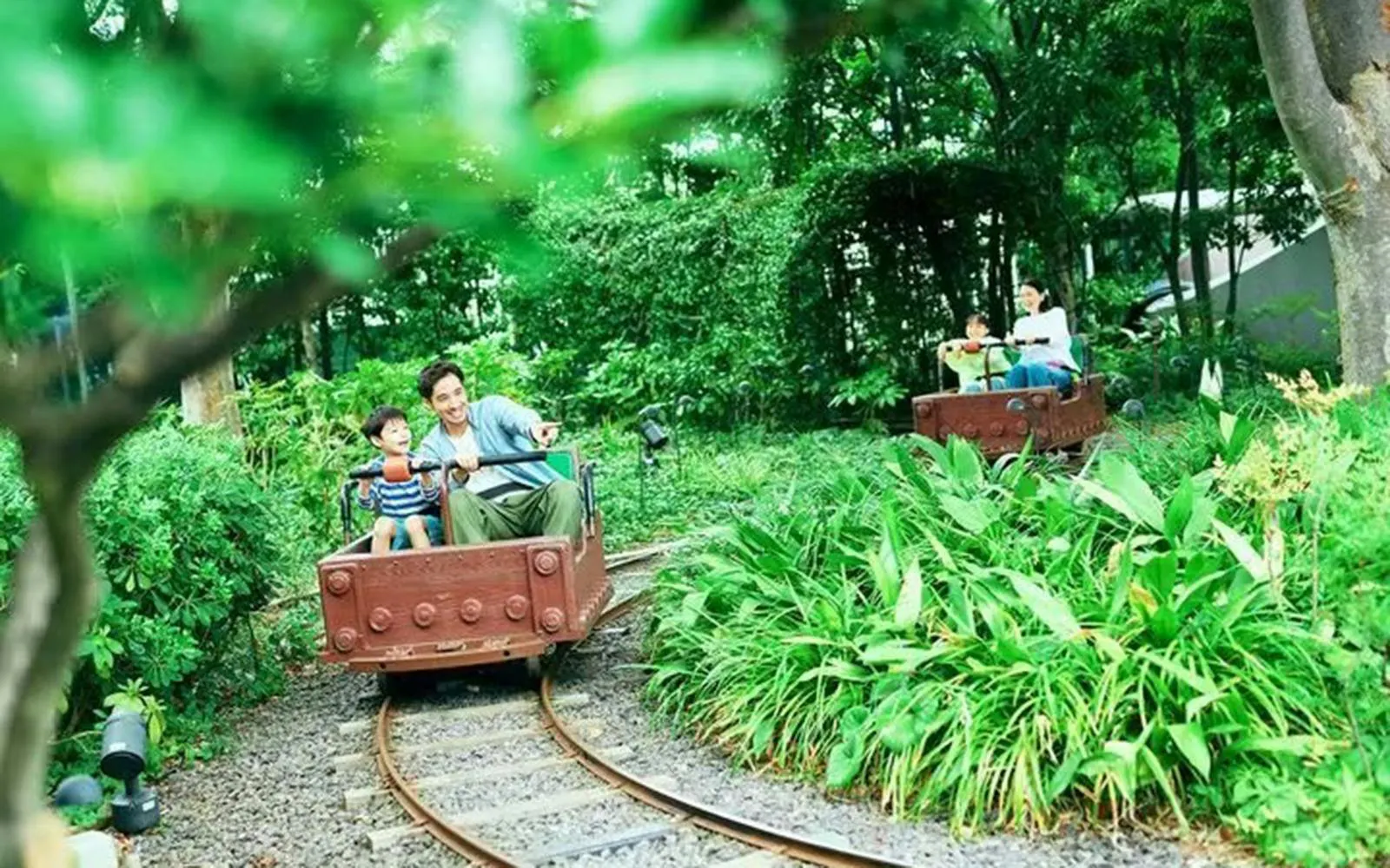 Father and son riding a mini train through greenery at Tokyo Dome City.