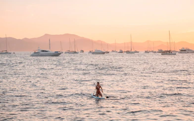 Paddleboarder on calm sea at sunset with yachts in French Riviera.