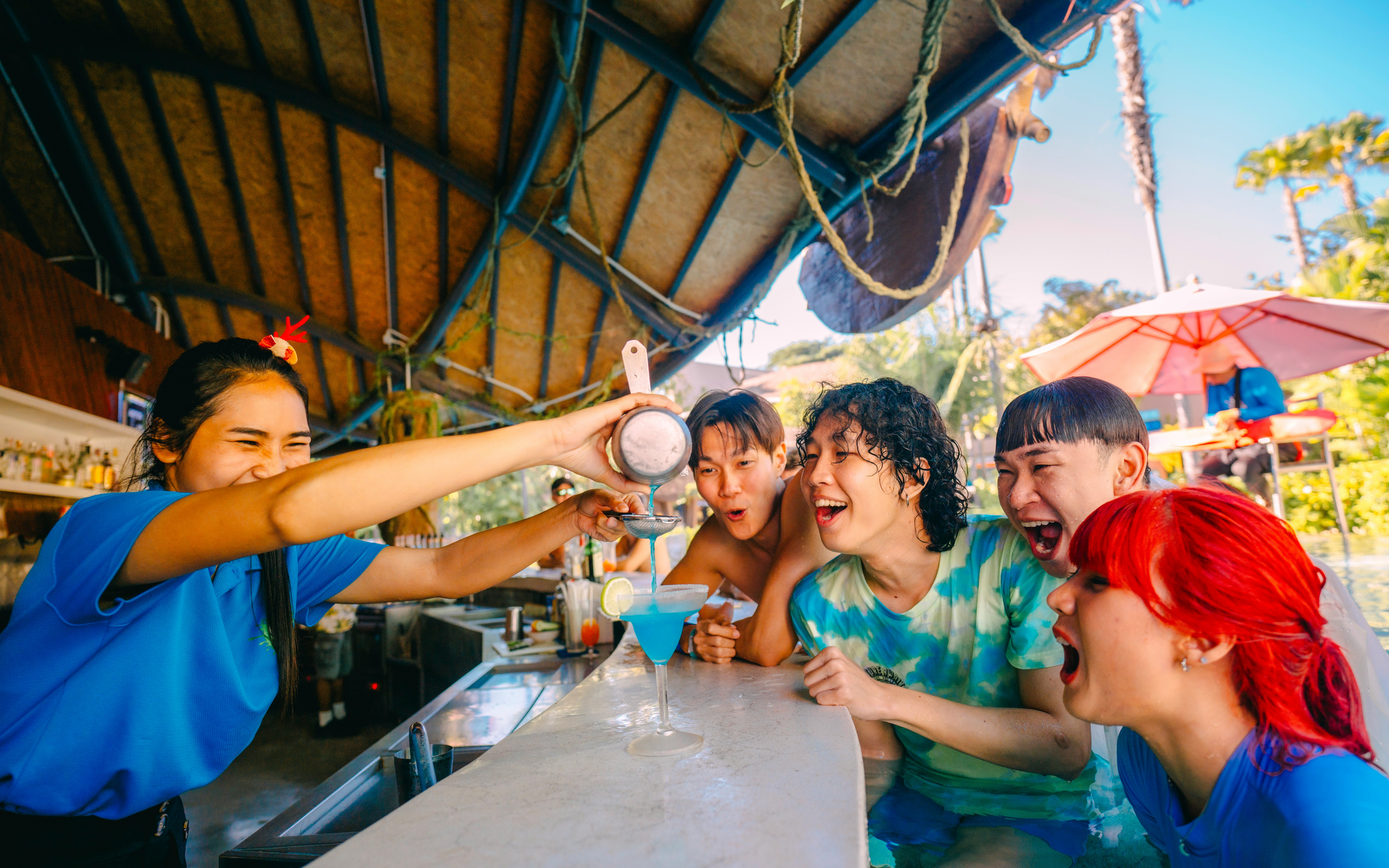 Bartender serving blue cocktail to excited group at Vana Nava Water Jungle bar.