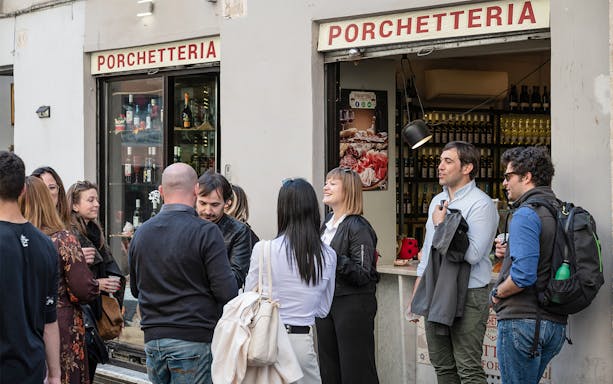 Group enjoying street food outside a porchetteria in Campo de' Fiori, Rome.