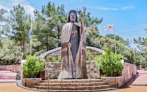 Monumental bronze statue of Makarios III in Troodos Mountains, Cyprus, with surrounding greenery.