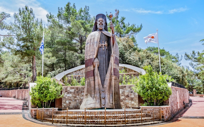Monumental bronze statue of Makarios III in Troodos Mountains, Cyprus, with surrounding greenery.