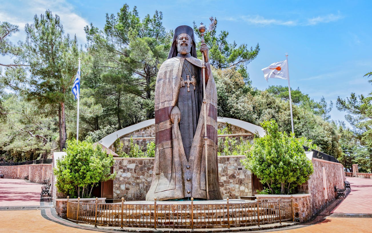 Monumental bronze statue of Makarios III in Troodos Mountains, Cyprus, with surrounding greenery.