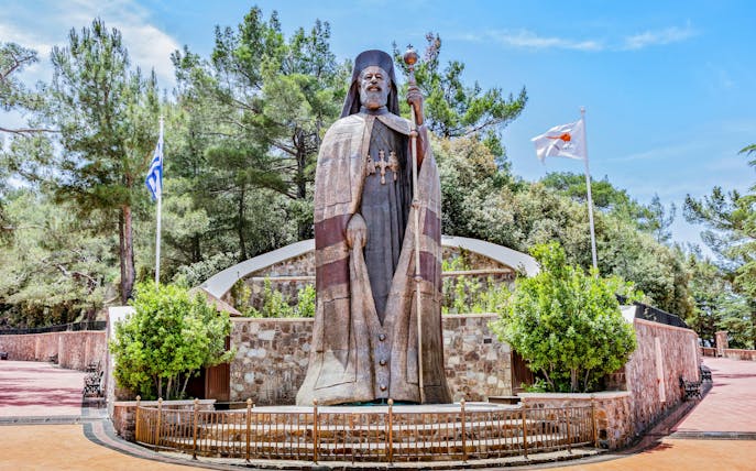 Monumental bronze statue of Makarios III in Troodos Mountains, Cyprus, with surrounding greenery.