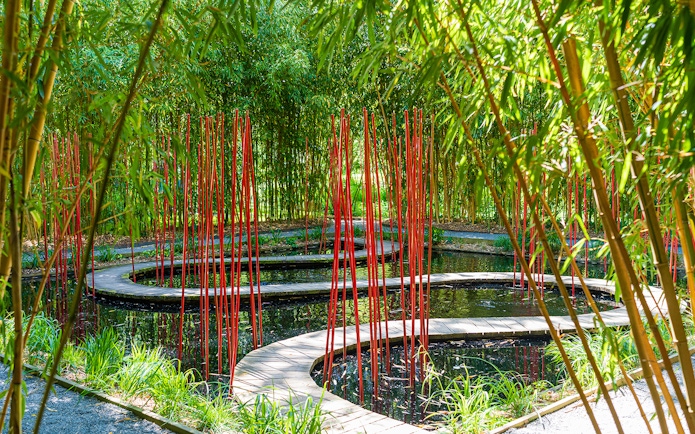 Curved wooden path with red poles in bamboo garden, Chaumont-sur-Loire Castle.