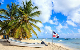 Boats on sandy beach with palm trees and Dominican Republic flag, Saona Island.