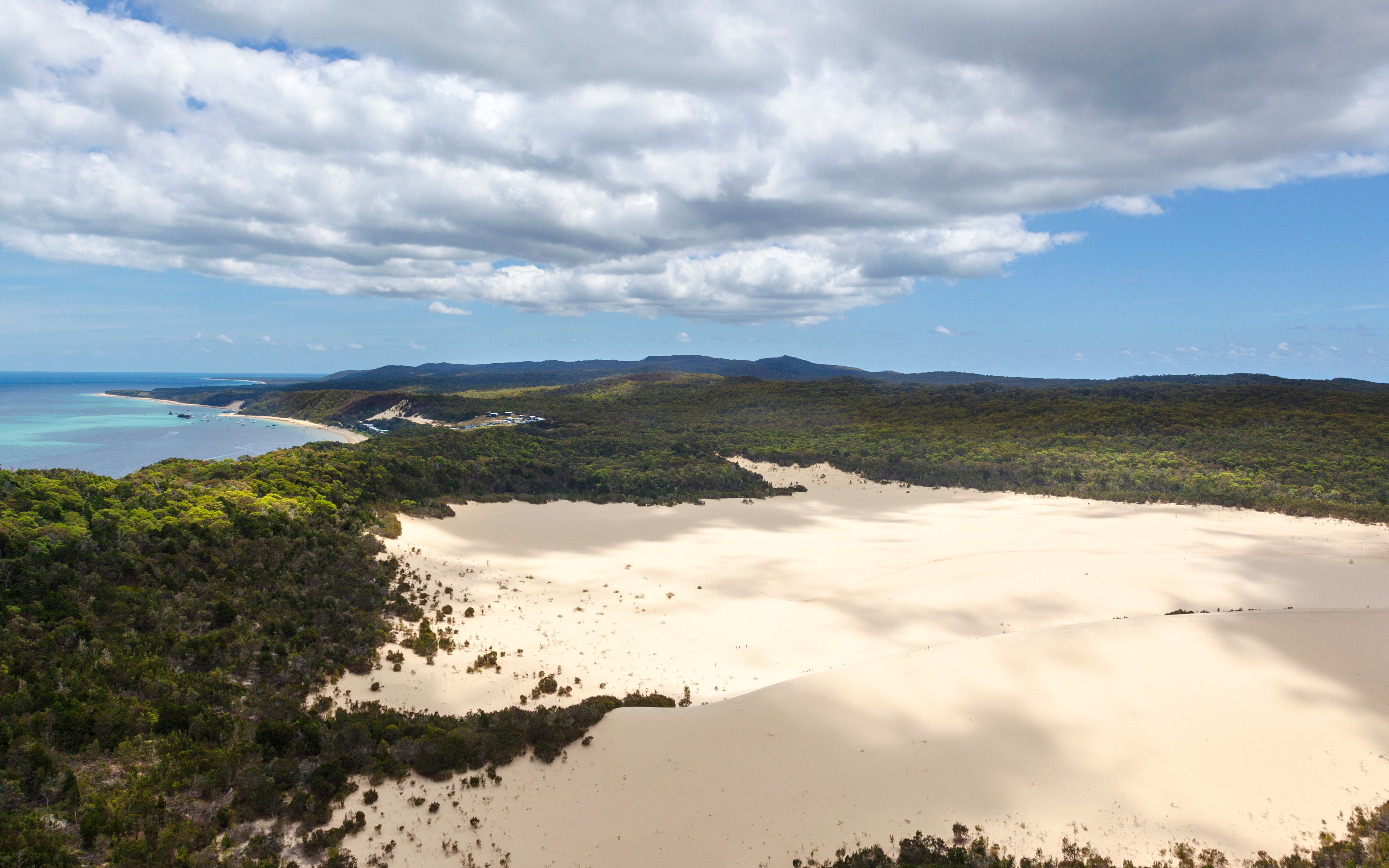 Sand dunes on Moreton Island with surrounding forest and coastline.