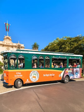 Old Town Trolley with passengers in San Diego near historic building.