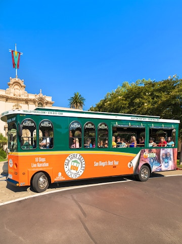 Old Town Trolley with passengers in San Diego near historic building.