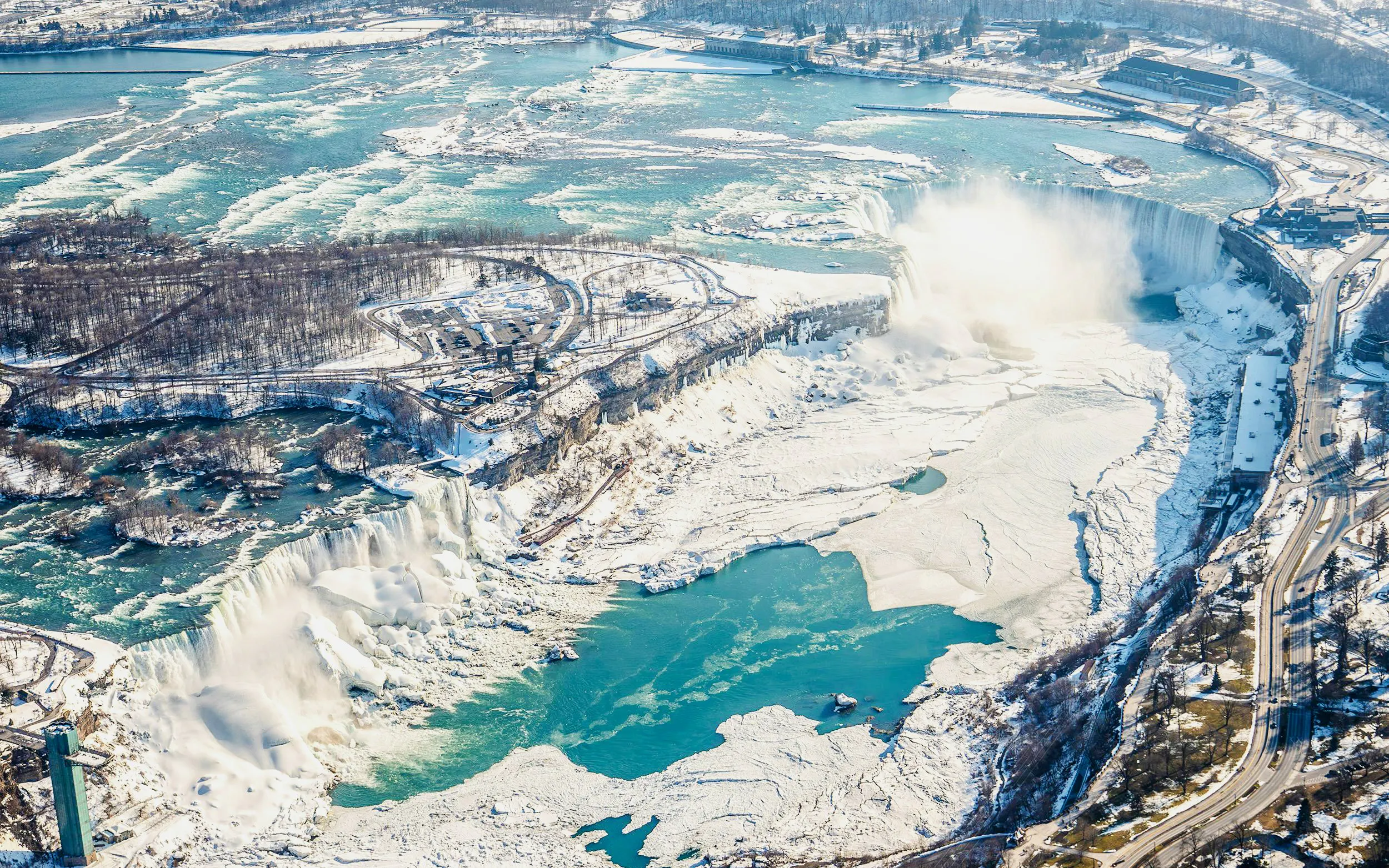 Aerial view of Niagara Falls in winter, showcasing frozen landscape and flowing water, Canada helicopter tour.