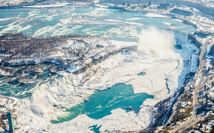 Aerial view of Niagara Falls in winter, showcasing frozen landscape and flowing water, Canada helicopter tour.