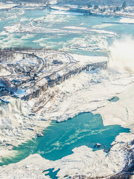 Aerial view of Niagara Falls in winter, showcasing frozen landscape and flowing water, Canada helicopter tour.
