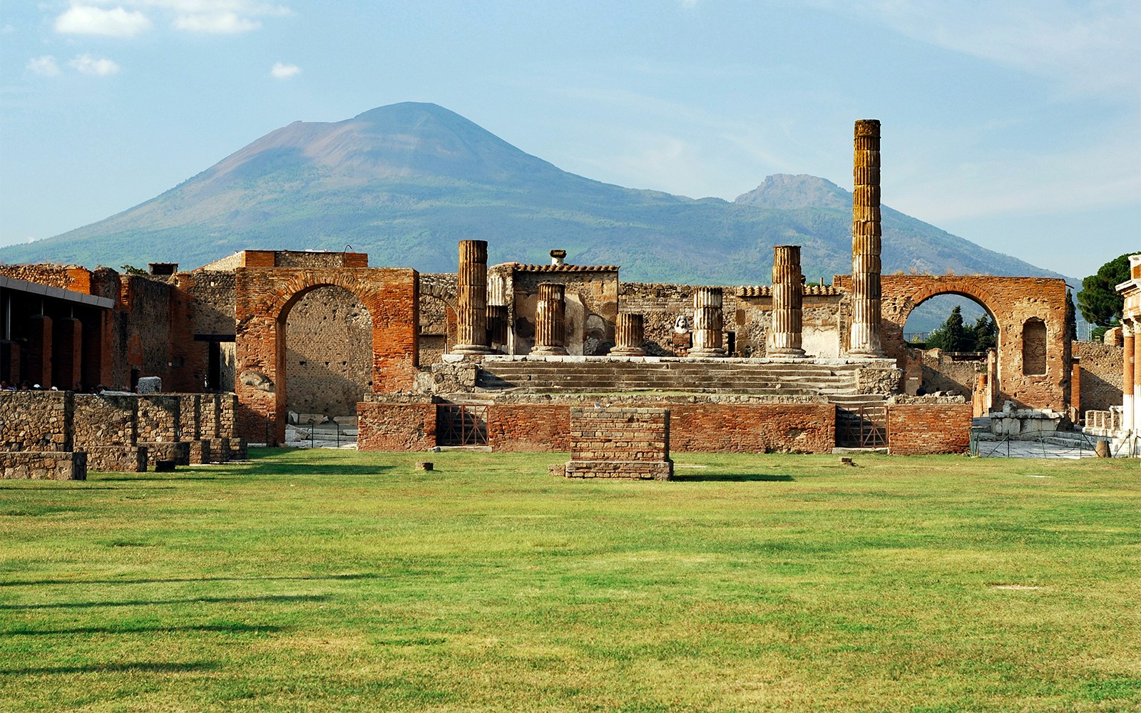 Tourists walking among ancient Pompeii ruins with Mount Vesuvius visible in the background, Italy.