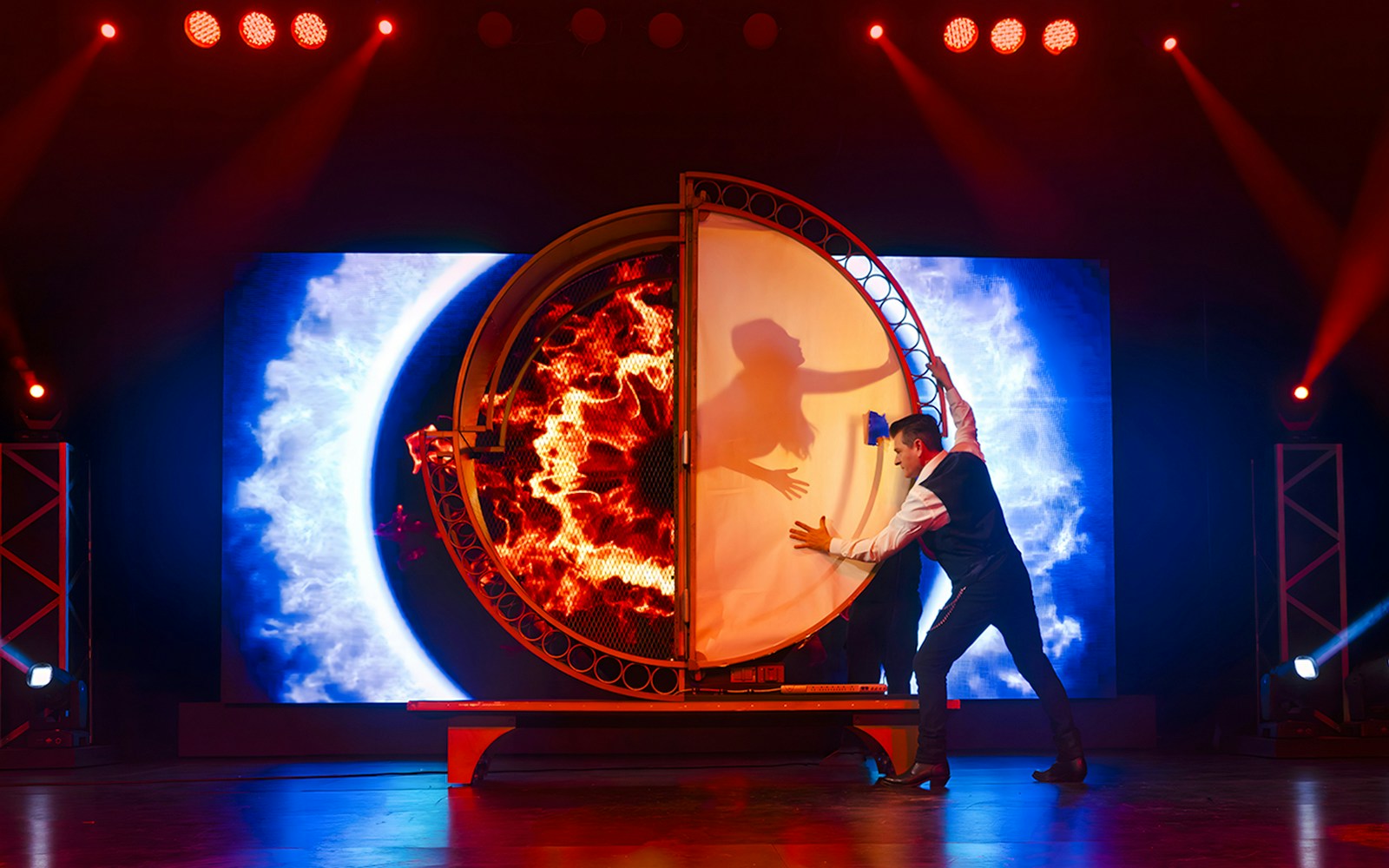 Magician performing illusion with fiery backdrop at Evolution Magic Show.