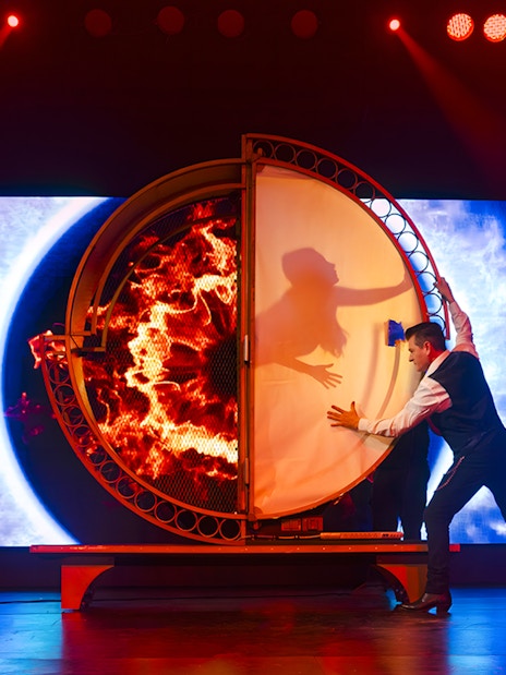 Magician performing illusion with fiery backdrop at Evolution Magic Show.