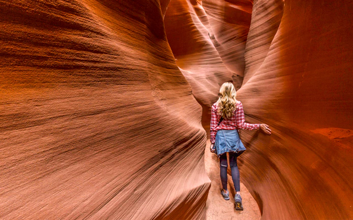 Person walking through narrow sandstone walls in Secret Antelope Canyon.