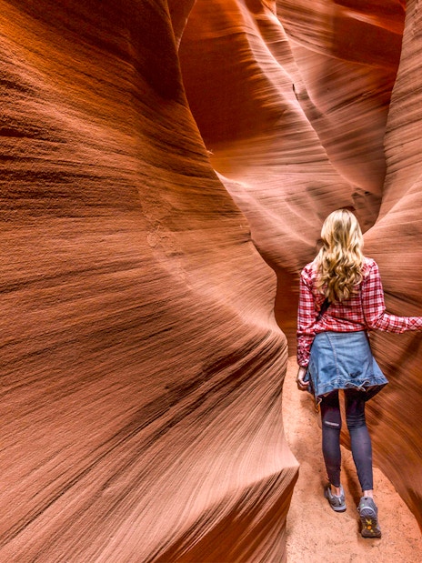 Person walking through narrow sandstone walls in Secret Antelope Canyon.