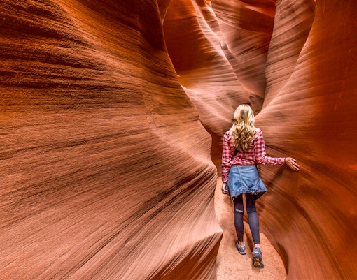 Person walking through narrow sandstone walls in Secret Antelope Canyon.