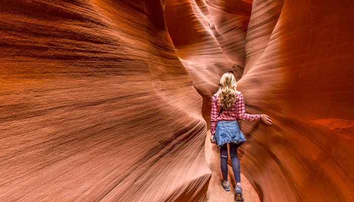 Person walking through narrow sandstone walls in Secret Antelope Canyon.