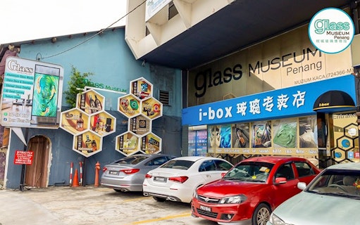 Glass Museum Penang entrance with colorful hexagonal displays and parked cars.