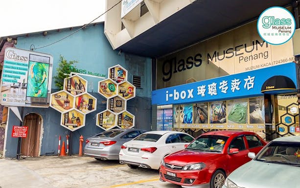 Glass Museum Penang entrance with colorful hexagonal displays and parked cars.
