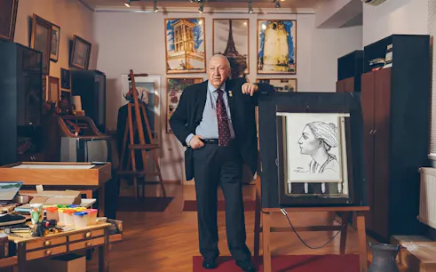 Man standing in art-filled room at House-Museum of Tahir Salahov, Baku, with portrait on easel.