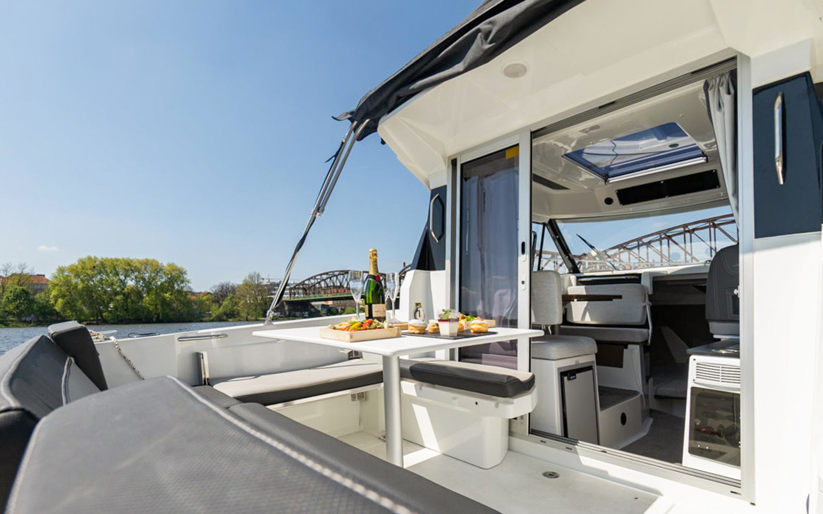 Prague yacht with table set for cruise, featuring drinks and snacks, with river and bridge view.