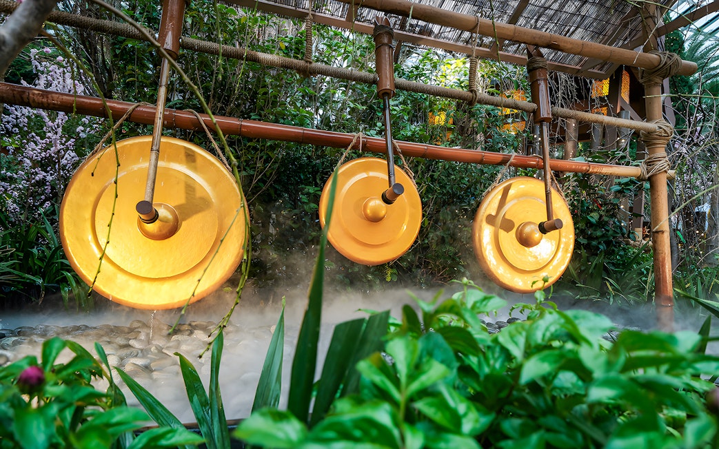Brass gongs in a lush garden setting at Gardens by the Bay with sakura blossoms.