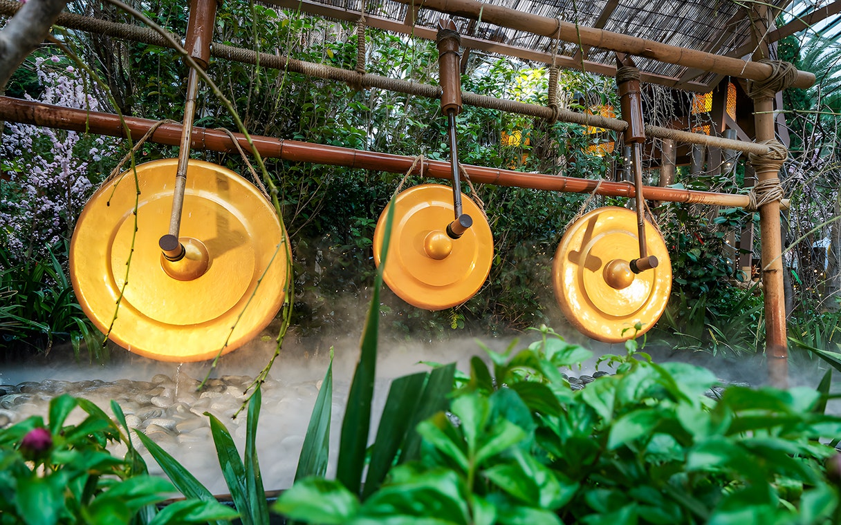 Brass gongs in a lush garden setting at Gardens by the Bay with sakura blossoms.