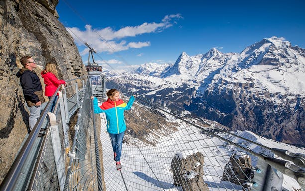 Visitors on a cliffside walkway with snowy Alps view at Schilthorn, Switzerland.