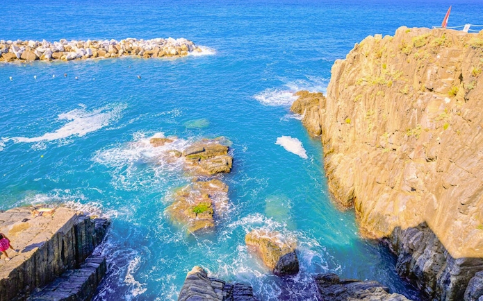Rocky coastline and clear blue sea in Cinque Terre, Italy, viewed from a cliff.