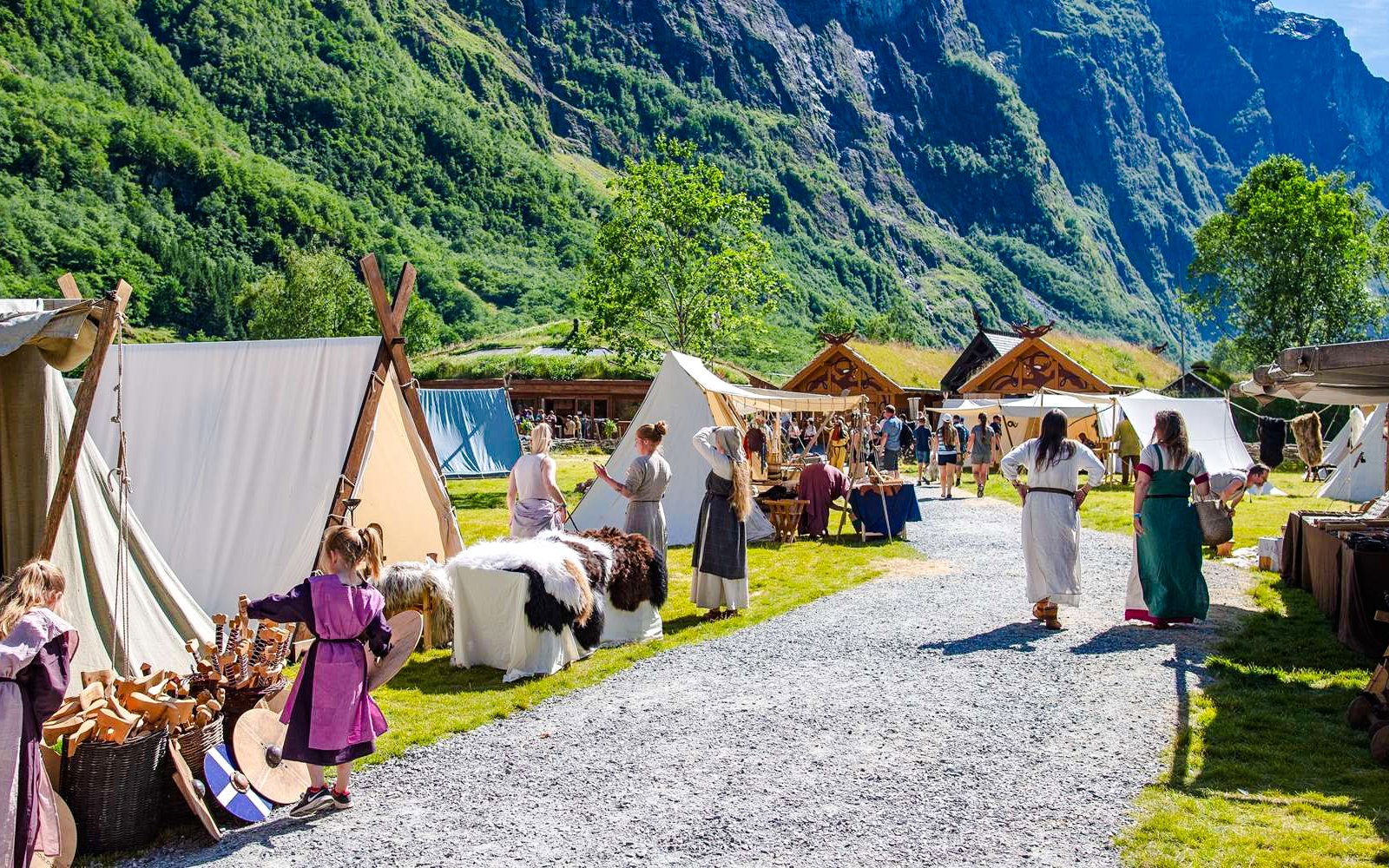 Viking reenactors in traditional attire at a Viking Village with tents and wooden huts.
