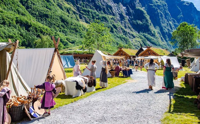 Viking reenactors in traditional attire at a Viking Village with tents and wooden huts.
