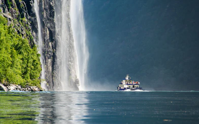 Boat cruising near a waterfall in Silent Fjord, Alesund, Norway.