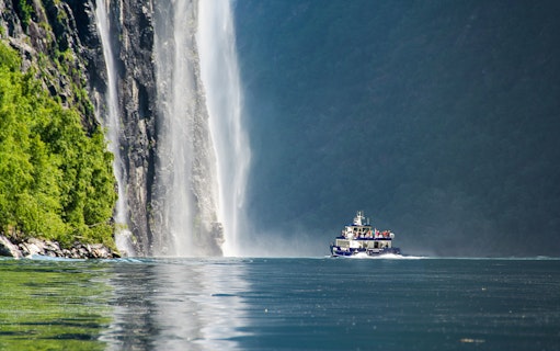 Boat cruising near a waterfall in Silent Fjord, Alesund, Norway.