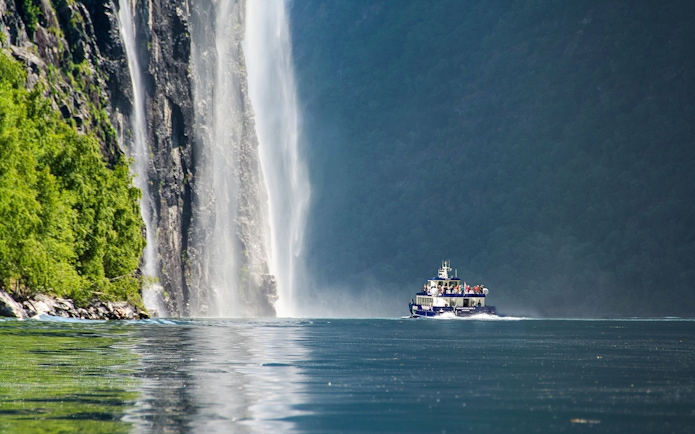 Boat cruising near a waterfall in Silent Fjord, Alesund, Norway.