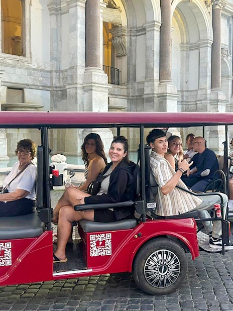 Tourists on a golf cart tour in front of a historic building in Rome.