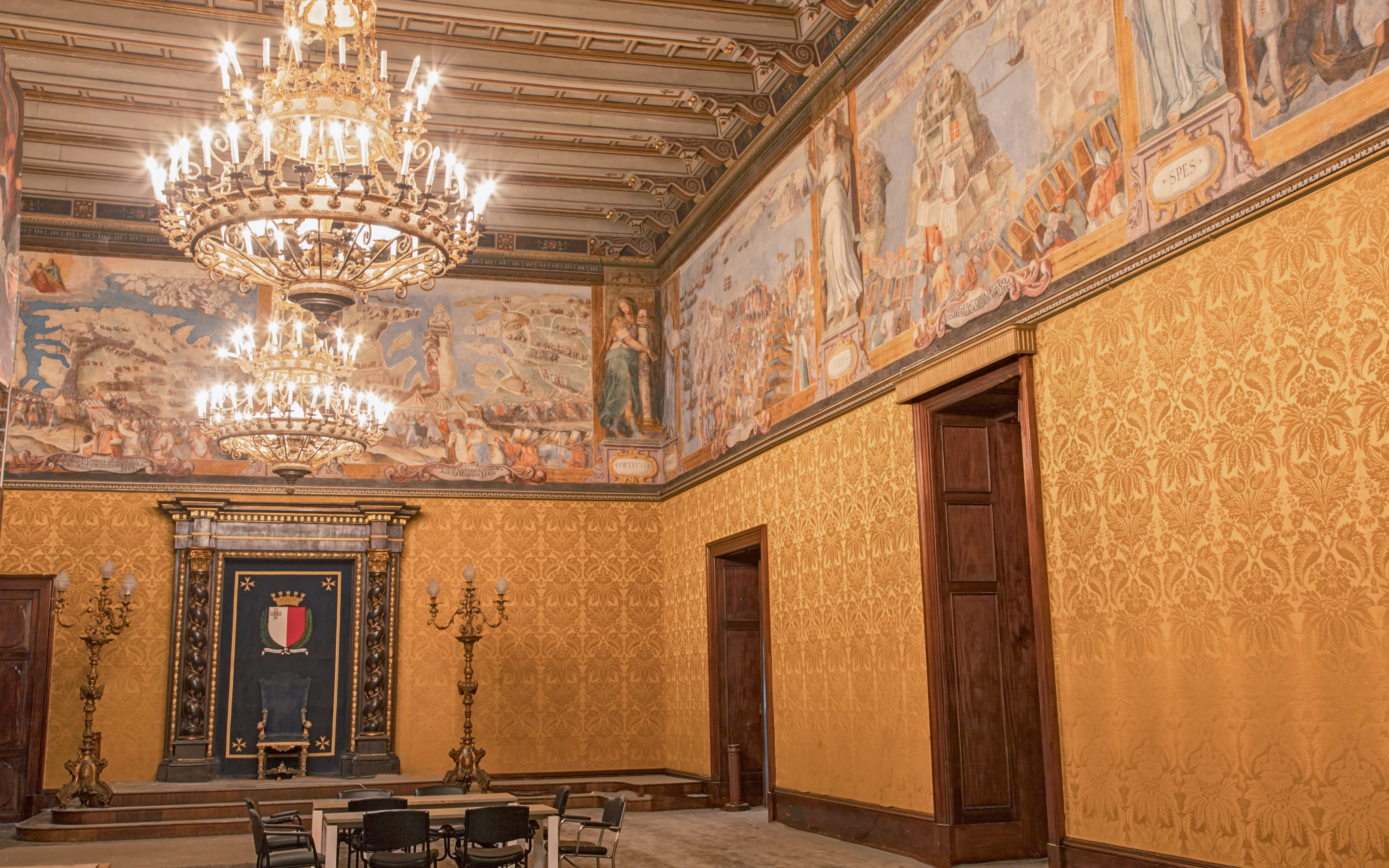 Grand hall with ornate chandeliers and historical frescoes in Malta's heritage site.