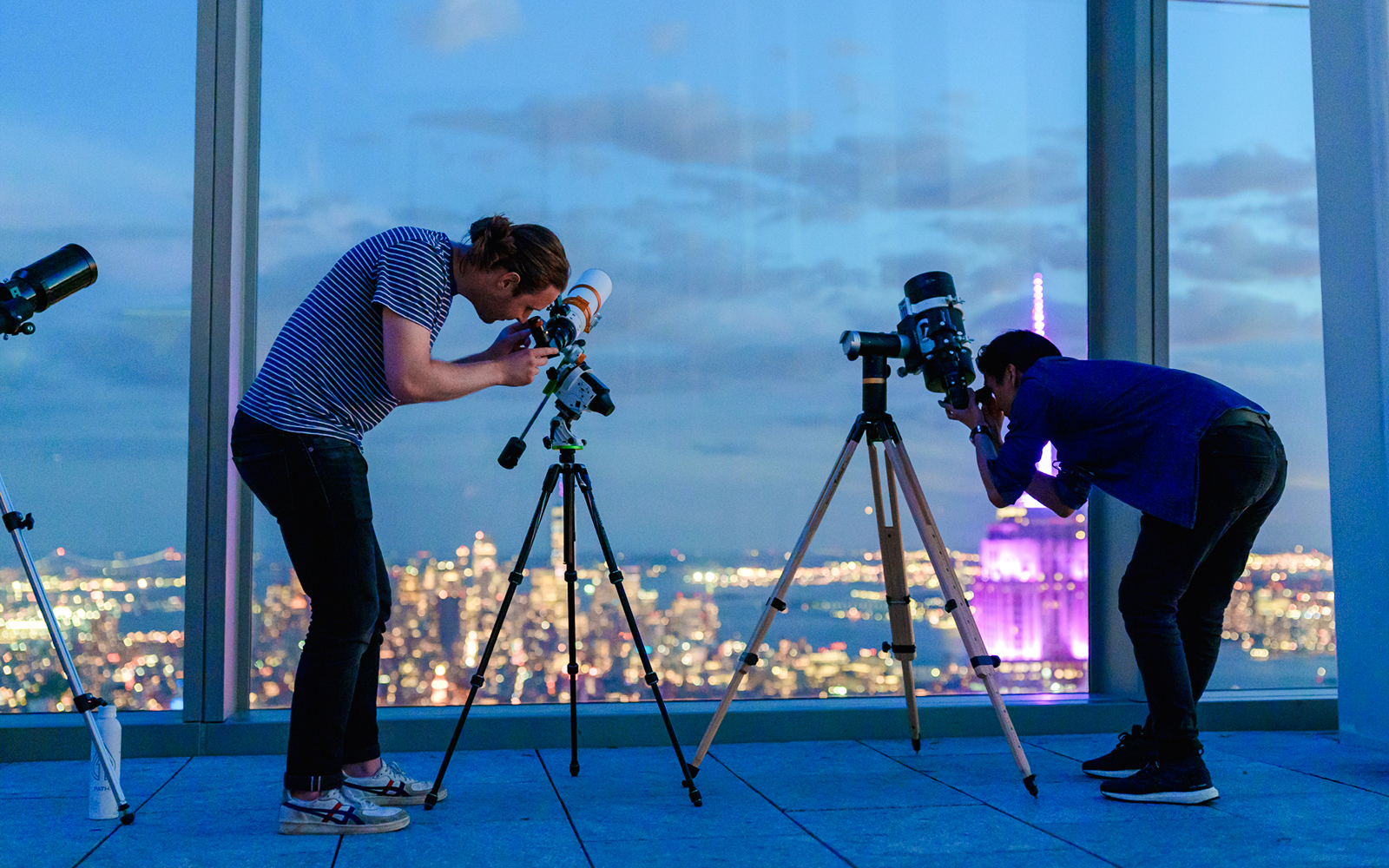 Visitors stargazing through telescopes at Summit One Vanderbilt, New York City skyline in the background.