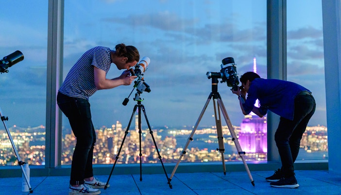 Visitors stargazing through telescopes at Summit One Vanderbilt, New York City skyline in the background.