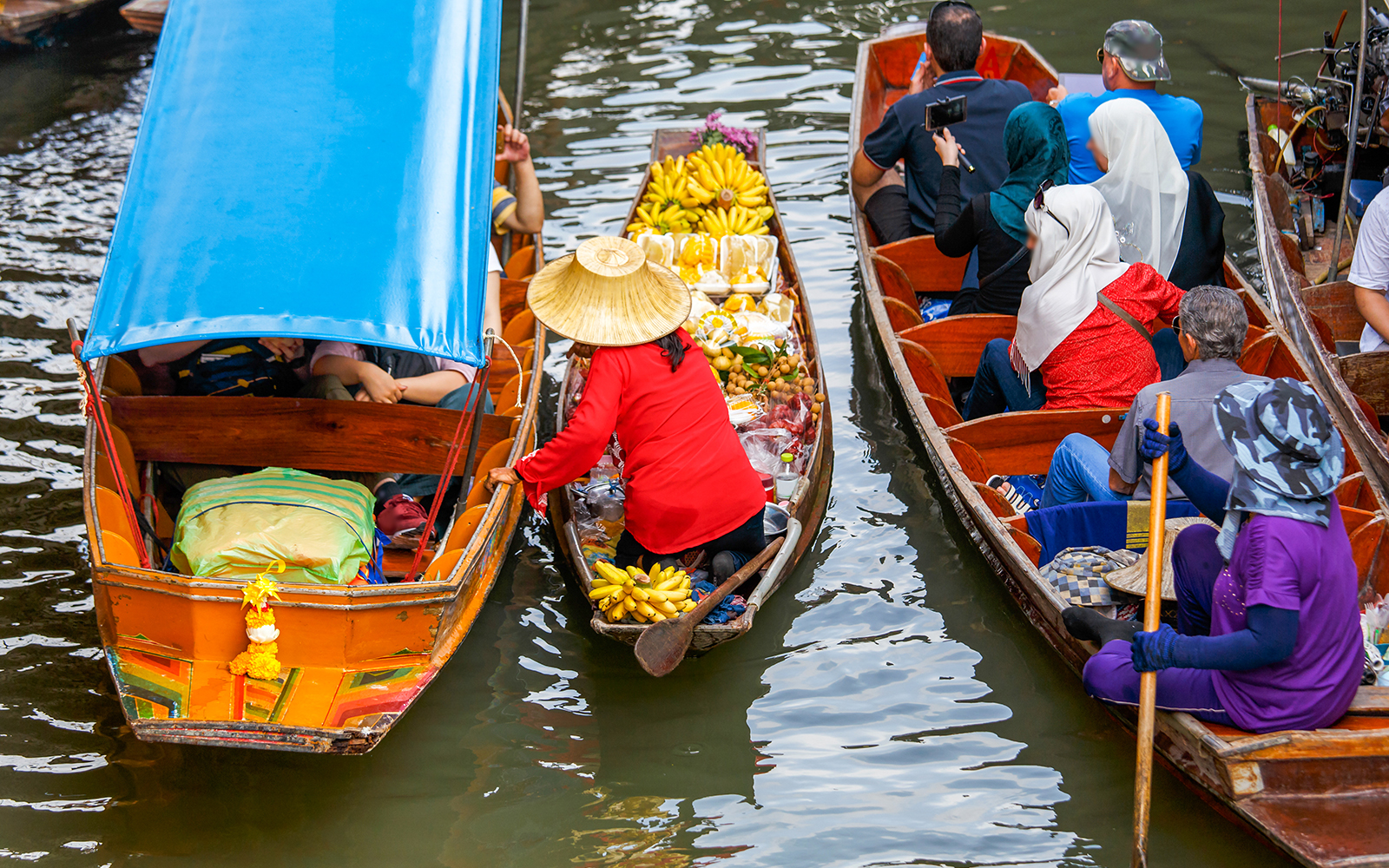 Vendors in straw hats sell bananas and other fruits from their boats at Damnoen Saduak Floating Market