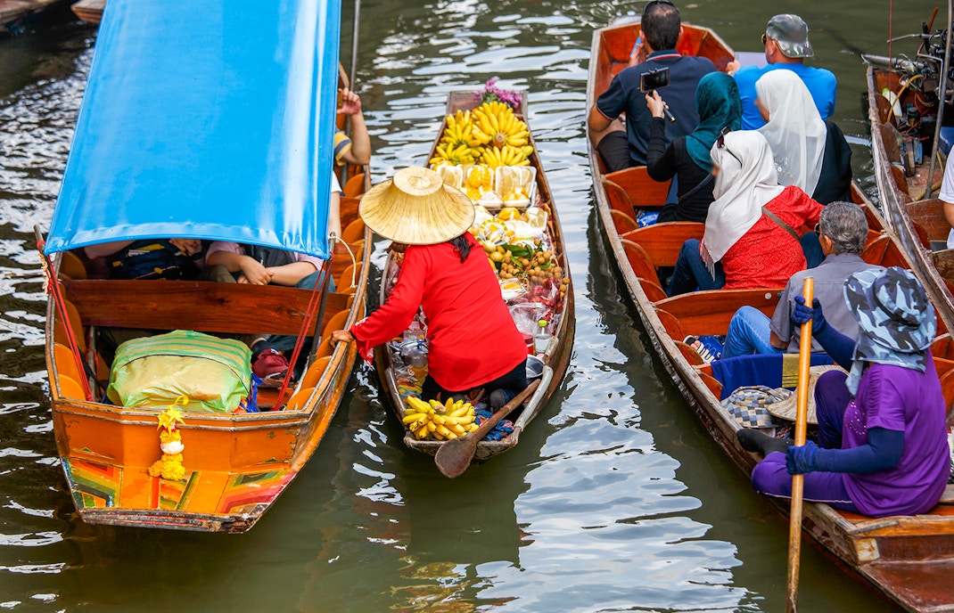 Vendors in straw hats sell bananas and other fruits from their boats at Damnoen Saduak Floating Market