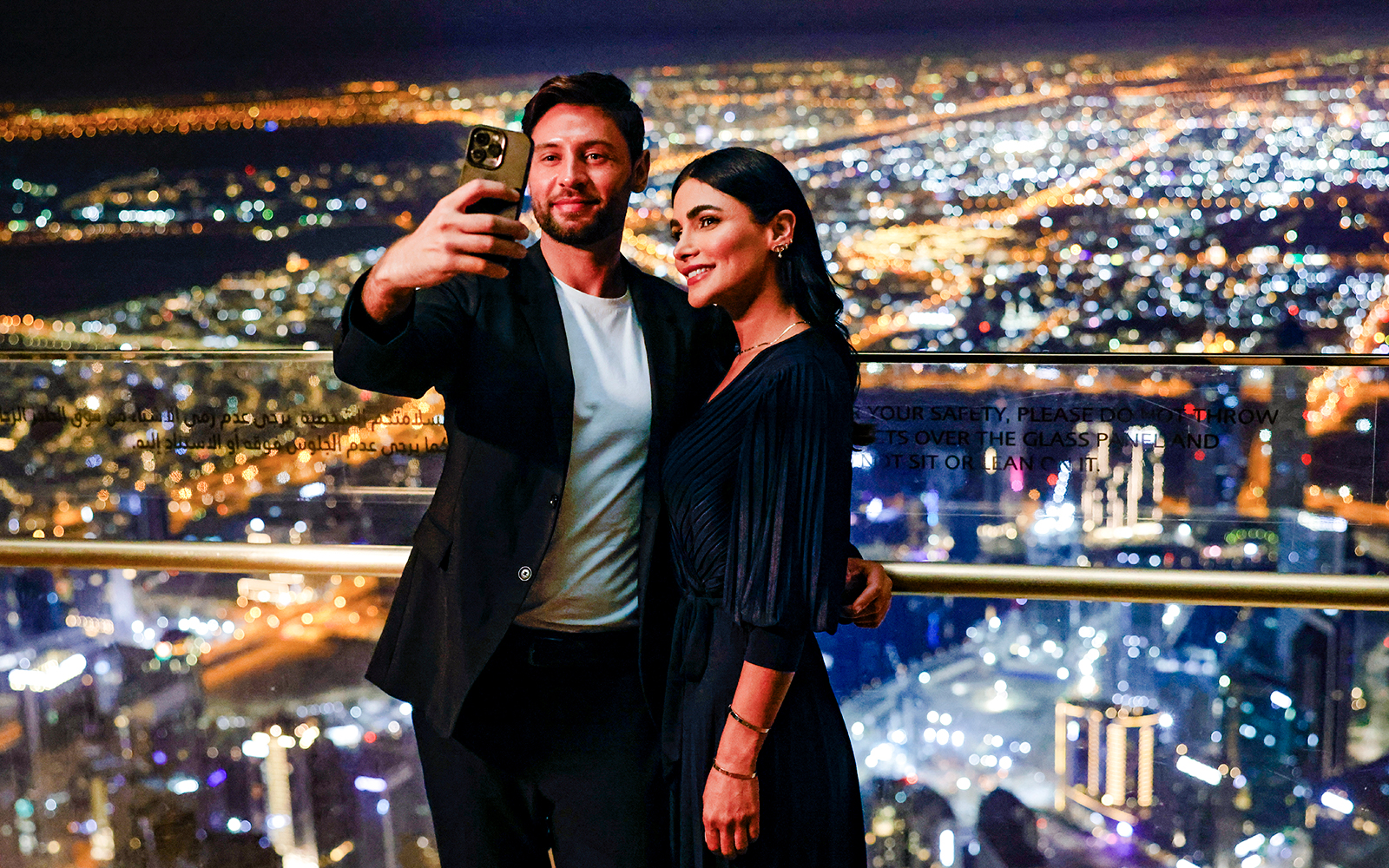 Couple taking selfie at Burj Khalifa Level 152 Lounge with Dubai city lights in background.