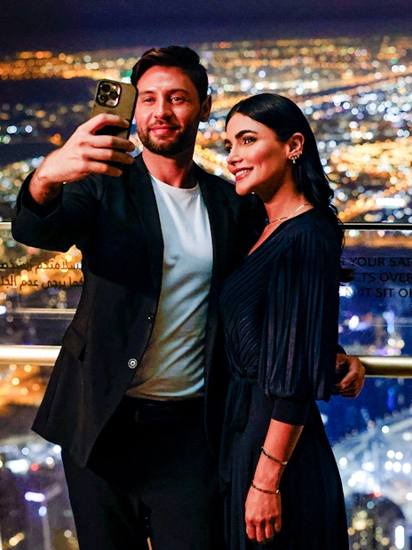 Couple taking selfie at Burj Khalifa Level 152 Lounge with Dubai city lights in background.
