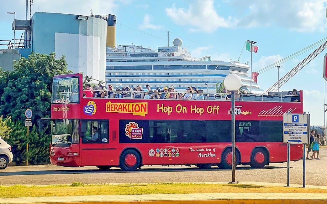 Heraklion Hop-On Hop-Off bus with tourists near a cruise ship.