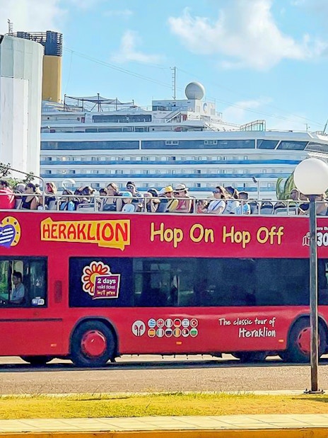 Heraklion Hop-On Hop-Off bus with tourists near a cruise ship.
